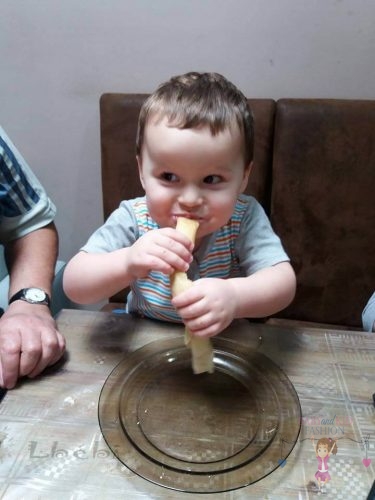 Babyandkidfashion, mosolygós kisfiú eszi a palacsinát, az általunk készített babaruhában, kép.