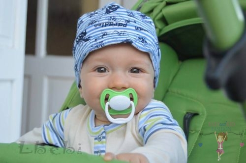 Babyandkidfashion, kisbaba mosolyog és cumizik a babakocsiban ülve, az általunk készített ruhában, kép.