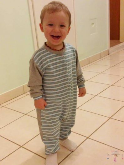 Gyermek kezeslábas pizsama,a képen egy 2 éves kisfiú mosolyog, az általunk készített kezeslábasban. A kezeslábas szürke-fehér-türkizkék csíkos, szürke hosszú ujjal, kép.