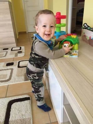 terepmintás babaruha, kisfiús terep mintás szett, egy mosolygós kisfiún, aki játékot tart a kezében, kép.