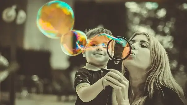 A család élete, anyuka ölében egy kisgyermek és nagy buborékot fújnak együtt, kép.