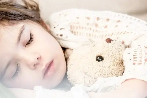 Szobatisztaság jelei, barna hajú kislány alszik és egy vajszínű mackót ölel magához, kép.