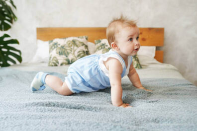 Babaágy után felnőtt ágy, felnőtt ágyon mászó kisgyerek, aki kék ruhában van, kép.